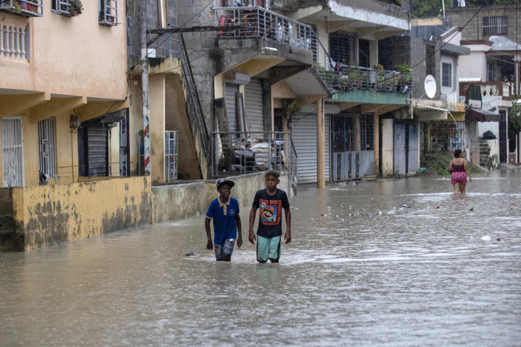 Personas caminan por una calle inundada en el barrio Manoguayabo este viernes, en Santo Domingo (República Dominicana). EFE/Orlando Barría